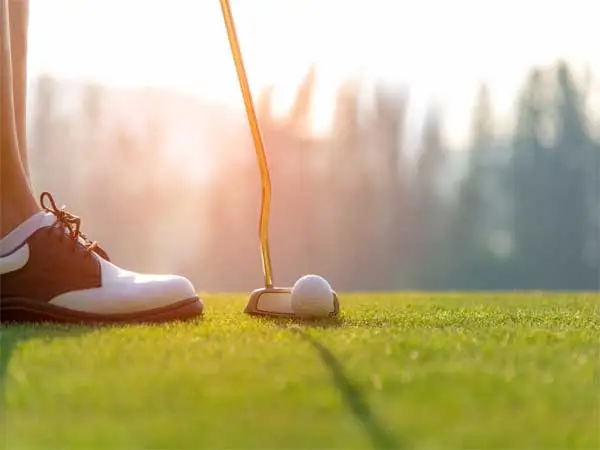 a golf club and a golf ball on a golf course with a man wearing spikeless golf shoes